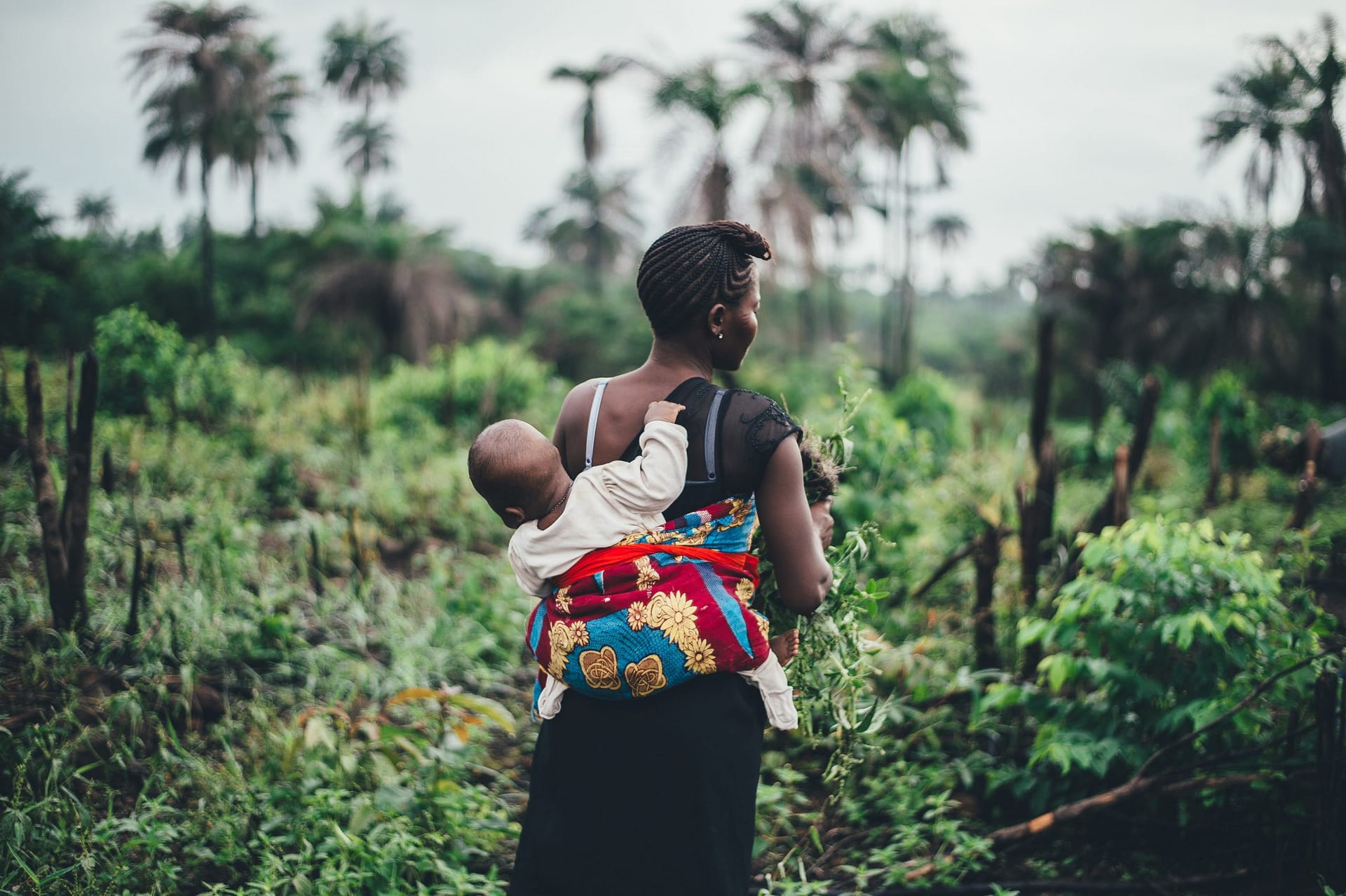 woman carries a baby near a tropical forest